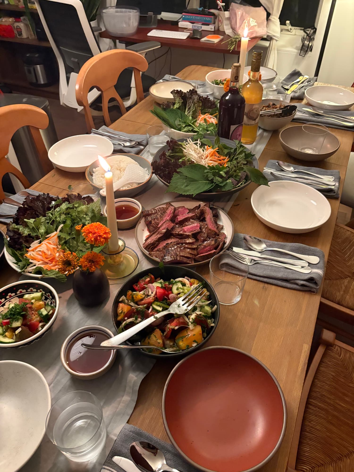 A fully set dinner table — skirt steak, salads, marigolds